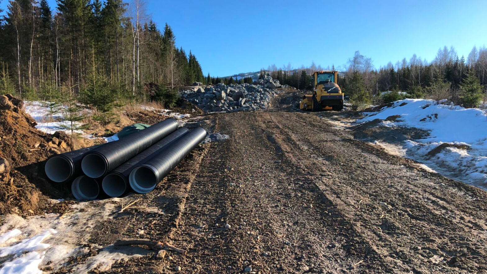 Bygging av skogsbilvei. viser maskin, stein til bruk i veien og rør.